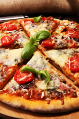 Vegetarian Italian pizza with melted cheese, red tomatoes and green basil on a table decorated by cheese, tomato and cherry tomatoes