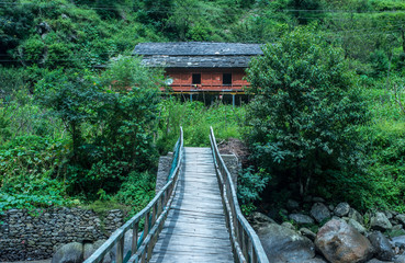 Wide view of a wooden bridge crossing a river bend leading to a house in himalaya, India