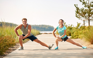 fitness, sport and lifestyle concept - smiling couple stretching legs on beach before training