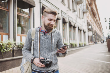 Outdoor portrait of cheerful young traveler man using smart phone on the street. Travel, tourism, active lifestyle concept