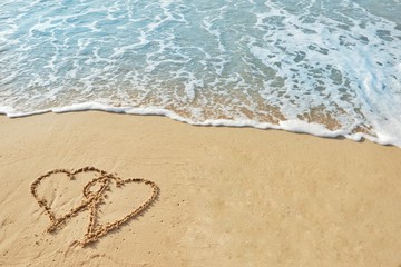 Valentine's day concept, two heart shape drawing on sand beach with wave ocean background.
