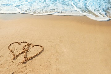 Valentine's day concept, two heart shape drawing on sand beach with wave ocean background.