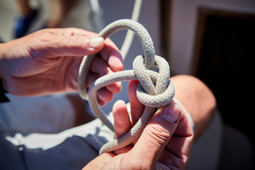Male hands tying knot on yacht sail boat - obrazy, fototapety, plakaty