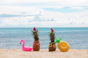 Family of funny attractive pineapples in stylish sunglasses on the sand against turquoise sea. Wearing christmas hats. Christmas and new year vacation concept on tropical beach. Family holiday. Bright