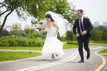 The bride and groom run together on the road in the summer