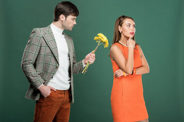 handsome man in vintage clothes presenting flowers to thoughtful woman isolated on green
