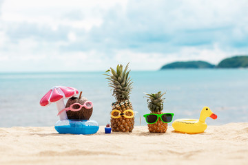  funny attractive pineapples and coconut in stylish sunglasses on the sand against turquoise sea. Wearing christmas hats. Christmas and new year vacation concept on tropical beach. Family holiday.