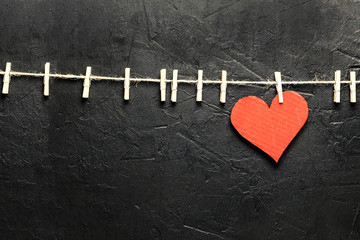 Valentine's Day. Red heart hanging on rope with copy space on black textured background