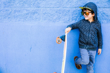 Little skater plays with the board on a blue wall