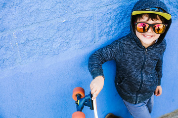 Little skater plays with the board on a blue wall