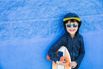 Little skater plays with the board on a blue wall