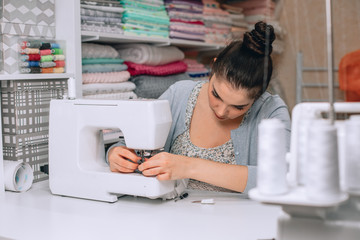 portrait of young woman seamstress sitting and sews on sewing machine. Tailor making a garment in her workplace. Hobby as a small business concept