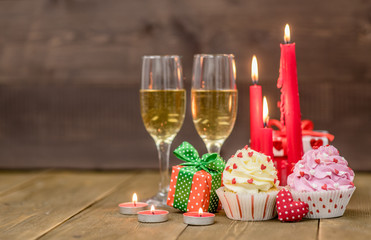 Pair glass of champagne with cupcakes, heart, gift box and candles. Wooden background with empty space for text