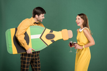 beautiful couple in vintage clothes with cardboard bottle and red wine glasses isolated on green