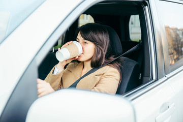 young woman driving car. safety belt. drinking coffee