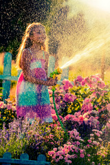 Summer fun, watering flowers - lovely girl has fun watering flowers in the garden