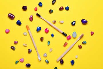 Eco natural bamboo toothbrushes on bright yellow background with colorful stones.