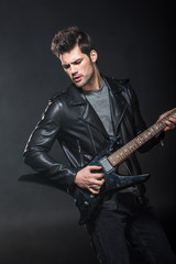 Obraz premium handsome rocker in leather jacket playing electric guitar isolated on black