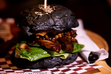 Juicy and greasy rustic burger with mayonnaise melting inside grilled roasted chicken meat and green lettuce with dark charcoal bun.