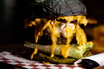 Obraz premium Juicy and greasy rustic cheese burger with mayonnaise melting inside grilled beef meat and lettuce with dark charcoal bun.