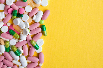 Medical theme. Multicolored pills, tablets and capsules on yellow background. Closeup.