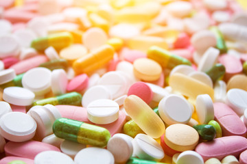 Medical theme. Multicolored pills, tablets and capsules on yellow background. Closeup. Selective focus.