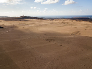 Fototapeta na wymiar Aerial view of a desert landscape on the island of Lanzarote, Canary Islands, Spain. Road that crosses a desert. Tongue of black asphalt cutting a desert land. Reliefs on the horizon. Volcanoes