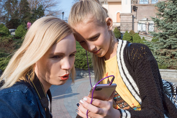Fototapeta premium The girl and mother look at the mobile phone on the street.