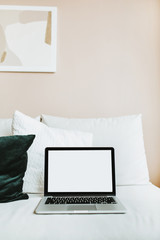 Minimal home office workspace. Laptop with mockup blank screen on bed with pillows. Blogger / freelancer business concept.