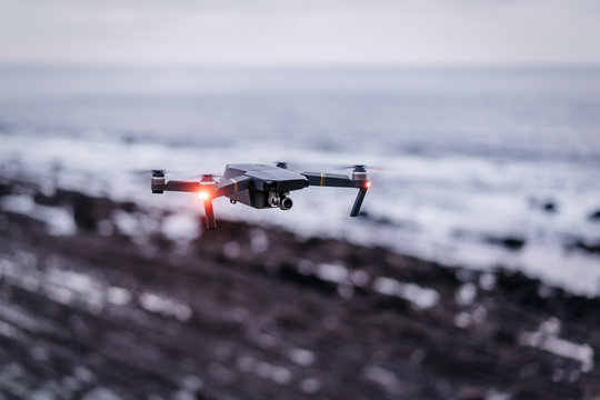 Modern drone with shining lights flying on blurred background of sea and coast