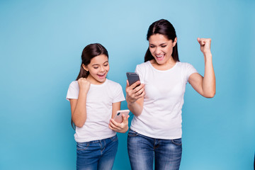 Close up photo beautiful two people brown haired mom small little daughter hold telephone reader great news fists in air win free sale discount wear white t-shirts isolated bright blue background