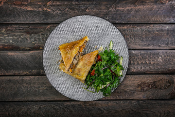 Strudel with stewed cabbage, meat and salad, served on the ceramic plate.