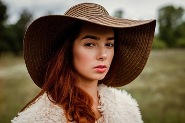 portrait of attractive young red haired woman in hat posing outdoors 