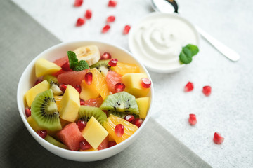 Tropical fruit salad in a white plate with sauce on a light background