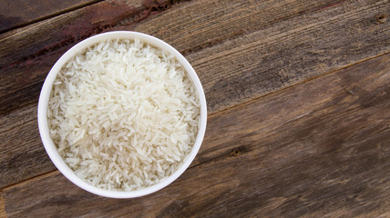 Dry rice in a white cup on a wooden background on top view.
