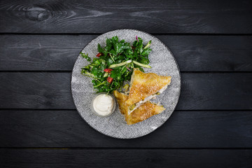 Strudel with chicken, zucchini and vegetable salad, served on the ceramic plate.