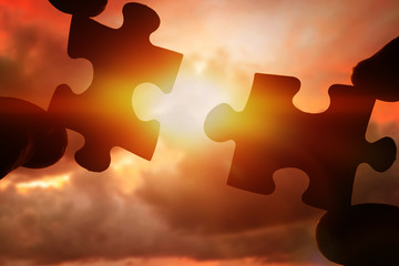 Puzzles in the hands of people at sunset, the evening sky. logic, interconnection, teamwork.