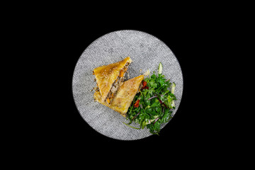 Strudel with stewed cabbage, meat and vegetable salad, served on the ceramic plate.