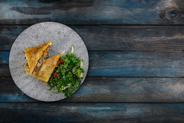 Strudel with stewed cabbage, meat and vegetable salad, served on the ceramic plate.