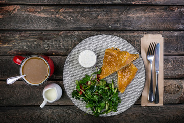 Strudel with mushrooms , cheese and vegetable salad, served on the ceramic plate with the cutlery and the cup of coffee.