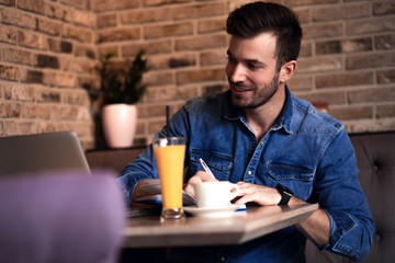 Young man sitting at cafe and working on laptop, casual businessman looking at computer.