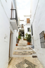 Small alley lane with white buildings and pots with flowers in front under a sunny sky in frigiliana spain