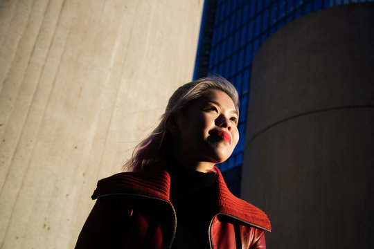 Edgy portrait of Asian woman wearing a red coat and red lips poses in warm urban environment