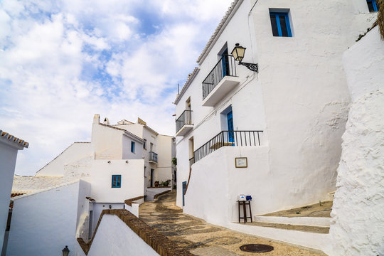 Stunning traditional architecture with white houses with blue windows and a small alley lane between under a sunny sky in frigiliana in spain