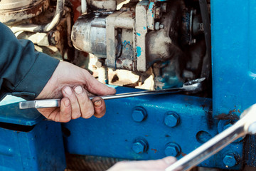 Farmer mechanic repairing tractor. Male hand holding wrench, repairing tractor engine.