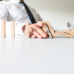 Businessman placing his hand to stop falling dominos
