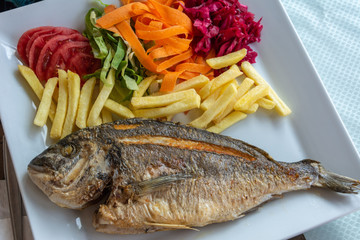 Plate of sea bream fish with French fries and salad