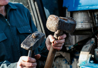 Male hand holding two big hammer, sledgehammer. Repairing tractor engine. Mechanic repairing tractor.
