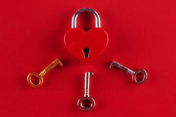 The concept of female infidelity. A heart shaped lock and three keys to it on a red background.