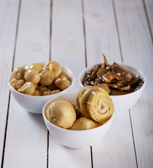 mushrooms and artichokes in oil in ceramic bowl on white wooden background.